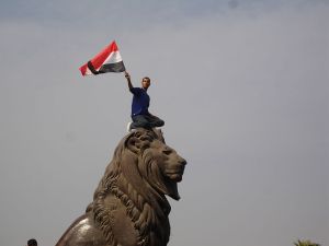 Man waving the egyptian flag on top of a Lion statue